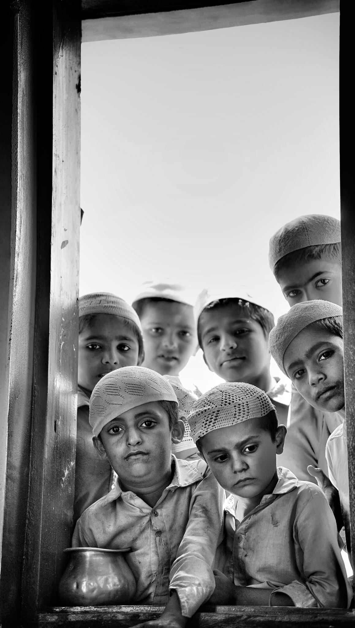 A group of children in traditional attire gazing through a window with solemn expressions.